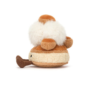 Side view of a Jellycat St. Honoré cake shaped plush with brown feet on a white background. 