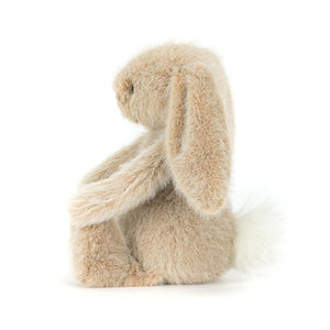 Side view of a Jellycat oat coloured bunny plush with a white fluffy tail on a white background.
