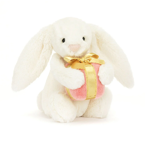 adorably soft plushie of a white bunny holding a pink and gold present by popular brand Jellycat.