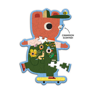 Finished puzzle in the shape and style of a skateboarding bear wearing green clothes with creatures  in the front pockets. The text 'cinnamon scented' is beside the puzzle. 