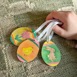 Hand holding three colourful Easter themed decorations hanging on ribbens.