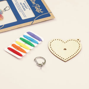 Heart-shaped wooden keychain kit with colorful strings and a silver keyring on a white background.