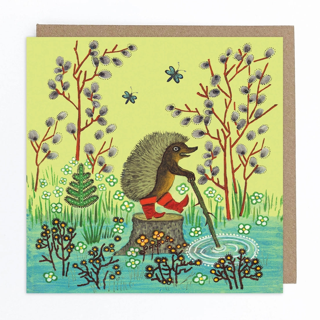Card featuring a folk art style illustration of a hedgehog standing on a tree stump, wearing red boots and holding a stick. The ground in front of the trunk is blue with some flowers growing. Two dragonflies fly in the background beside some trees. 