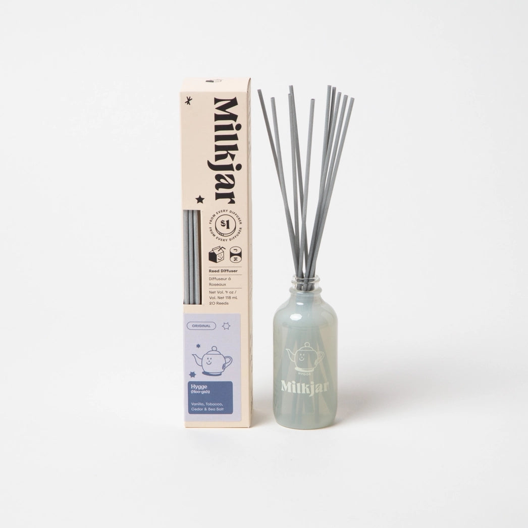 Milkjar diffuser bottle containing reed sticks beside packaging with the company branding on a white background