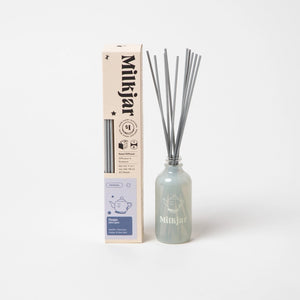 Milkjar diffuser bottle containing reed sticks beside packaging with the company branding on a white background