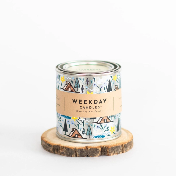 silver tin candle with nature and cottage painted doodles. a brown tag wraps the tin. on it, "Weekday Candles 100% Soy Wax Candle", the name of the product, the ingredients and instructions are written in a sharp black font.