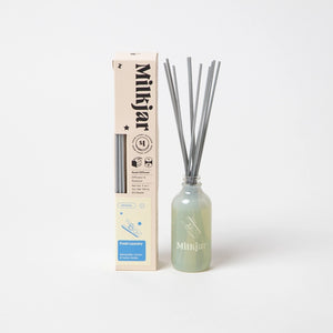 Milkjar diffuser bottle containing reed sticks, placed beside packaging on a white background