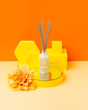 Glass container with reeds placed on a stand against an orange background.