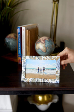 Hand holding a photo frame cotton card with a blue, green and gold botanical design in a home setting. The text 'Happy Birthday To You' is printed on the card. 