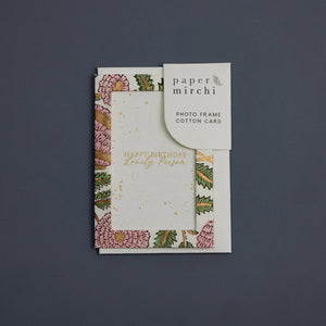 Photo frame cotton card with a pink and gold botanical design and 'Happy Birthday Lovely Person' text. The card sits on a blue background. 