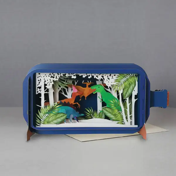 blue bottle pop up card. the intricate paper cuttings depict a white forest scene with dinosaurs. a raptor wears a party hat