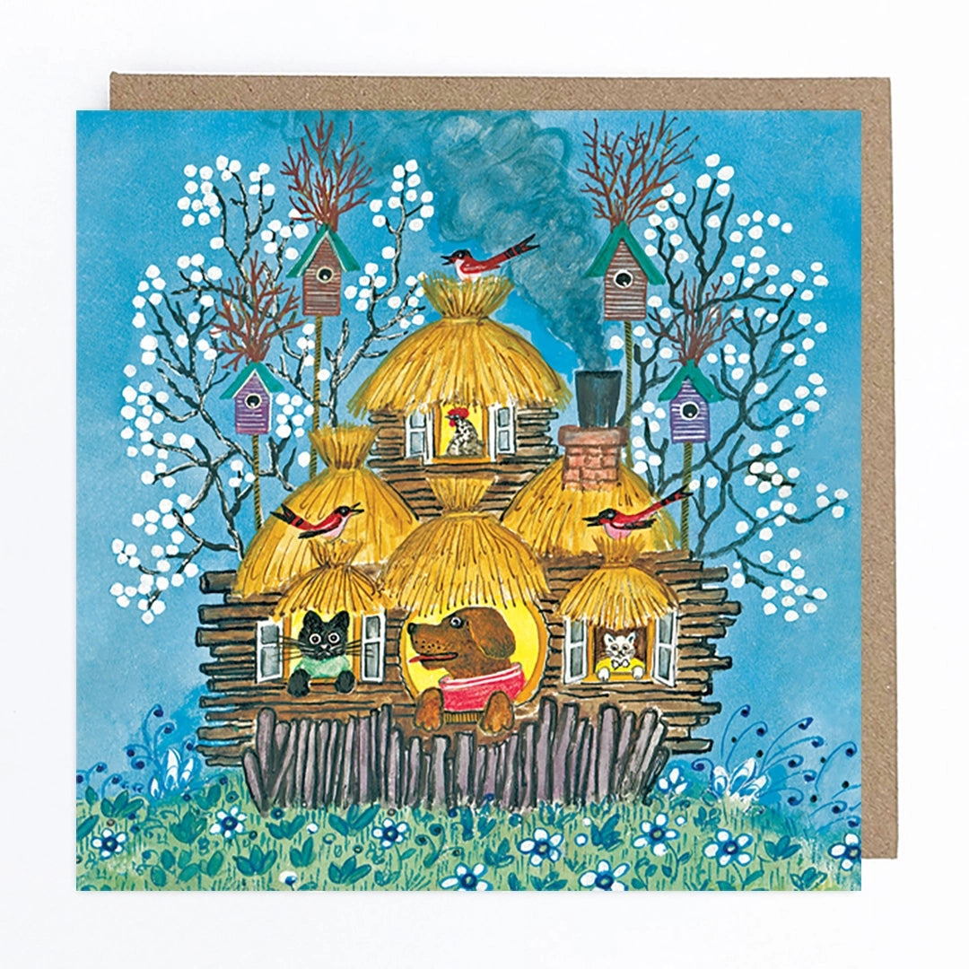 Card featuring a folk art style illustration of a dog, cats and a hen looking out the windows of a house with a straw roof. Behind the house, there are 4 birdhouses and trees, along with some birds perched on the roof against a blue background. 