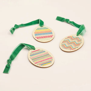 Three wooden ornaments with colorful patterns and green ribbons on a light background