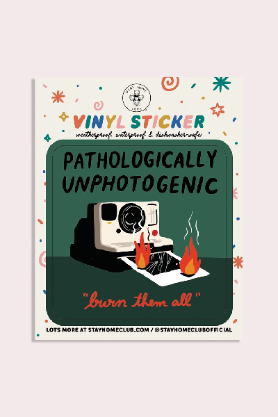 green sticker with a white polaroid camera and a burning picture coming out of it. top text reads "pathologically unphotogenic". bottom text reads "burn them all"
