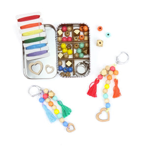 Open container filled with coloured beads and threads, beside two beaded keychains on a white background. 