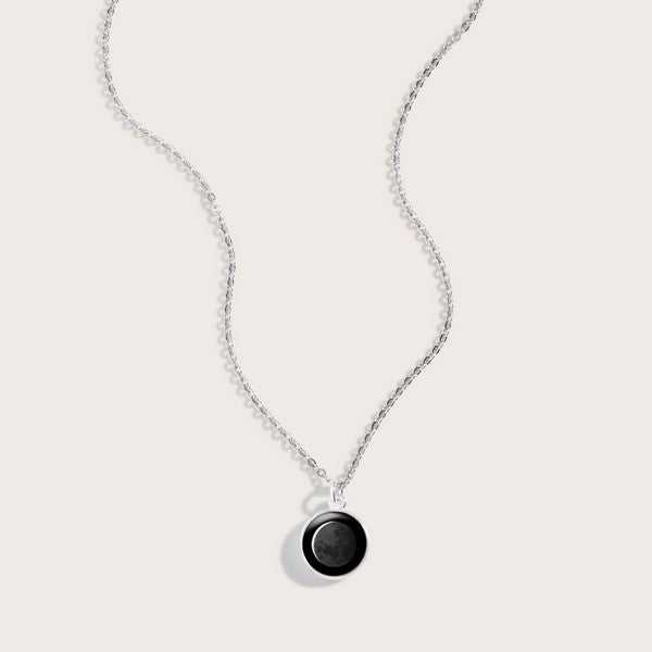 black circle pendant connected to a delicate silver chain. the pendant has an image of the moon in it