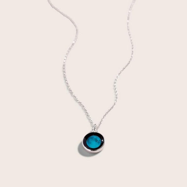 black circle pendant connected to a delicate silver chain. the pendant has a lit up, blue image of the moon in it