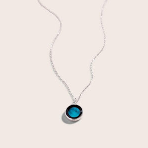 black circle pendant connected to a delicate silver chain. the pendant has a lit up, blue image of the moon in it