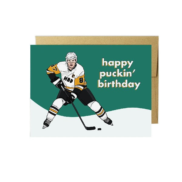 green and white birthday card with a hockey player with "HBD" on his white, black, and orange jersey. right side text reads "happy puckin' birthday"