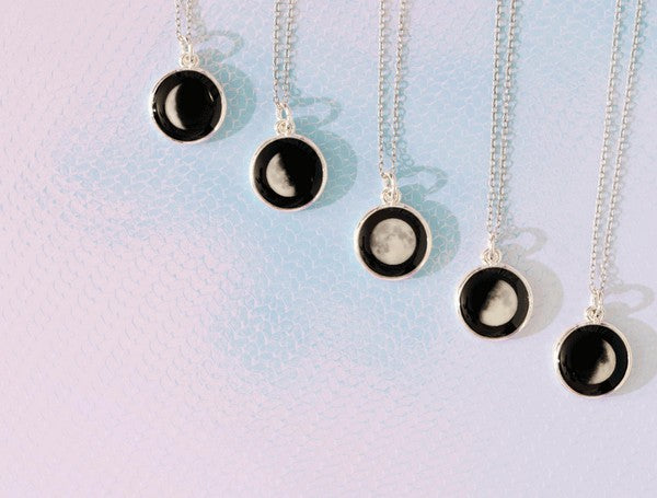 5 ends of necklaces. each of them has a black circle pendant connected to a delicate silver chain. the pendants depict an example of each phase of the moon (other than the new moon)