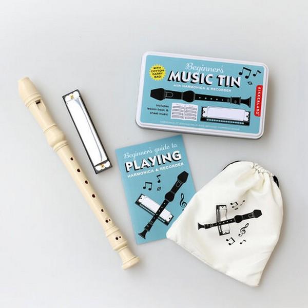 blue rectangular metal tin with its contents outside of it. main text on the package reads "beginner's music tin". outside contents include a beige plastic recorder, a metal harmonica, an off-white satchel with an illustration of the two instruments on it, and an instruction manual. kikkerland product on light grey background